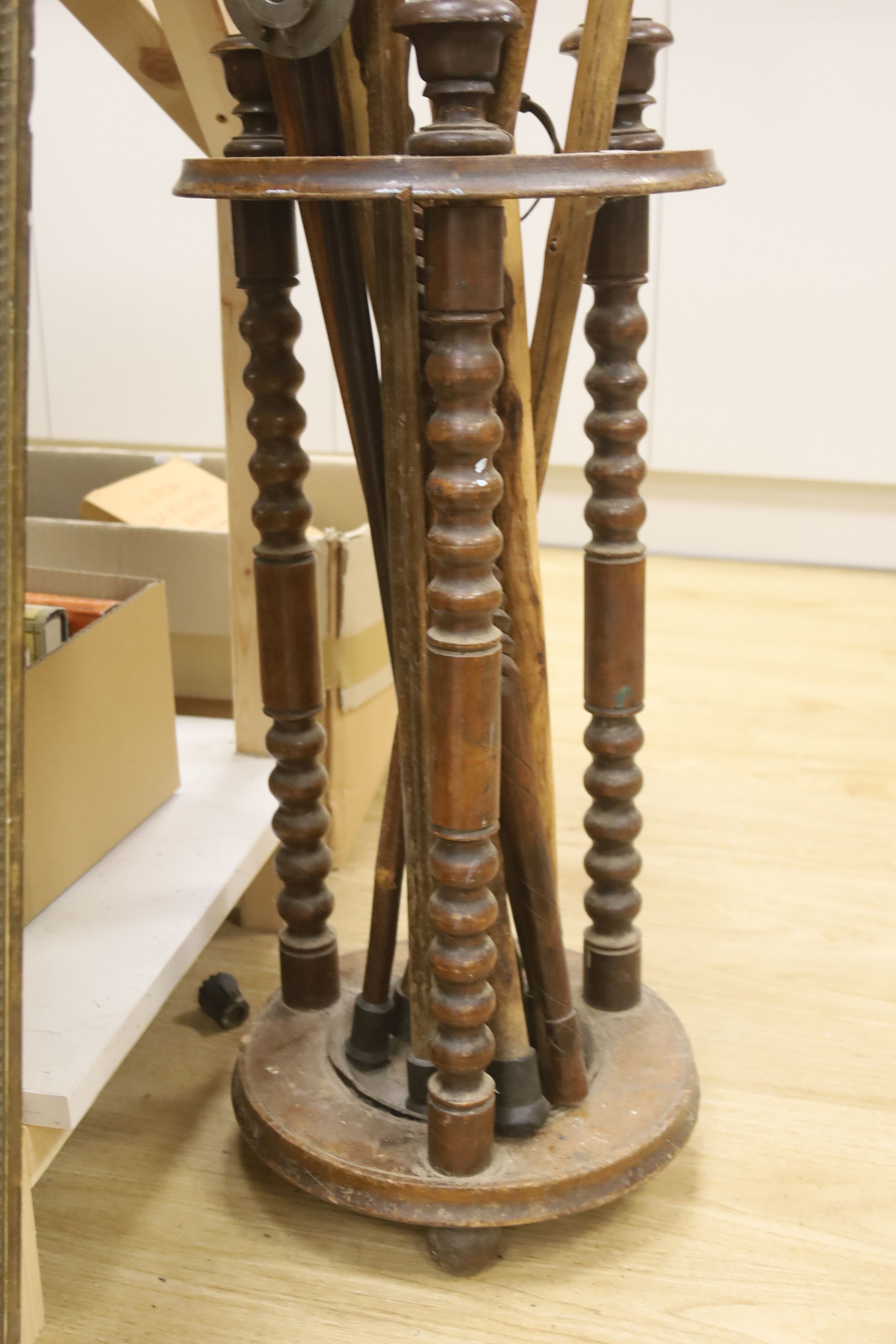 A circular turned beech stick stand, containing various walking sticks and a shooting stick